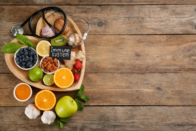 Photo of Card with phrase Immune System, stethoscope and fresh products on wooden table, flat lay. Space for text