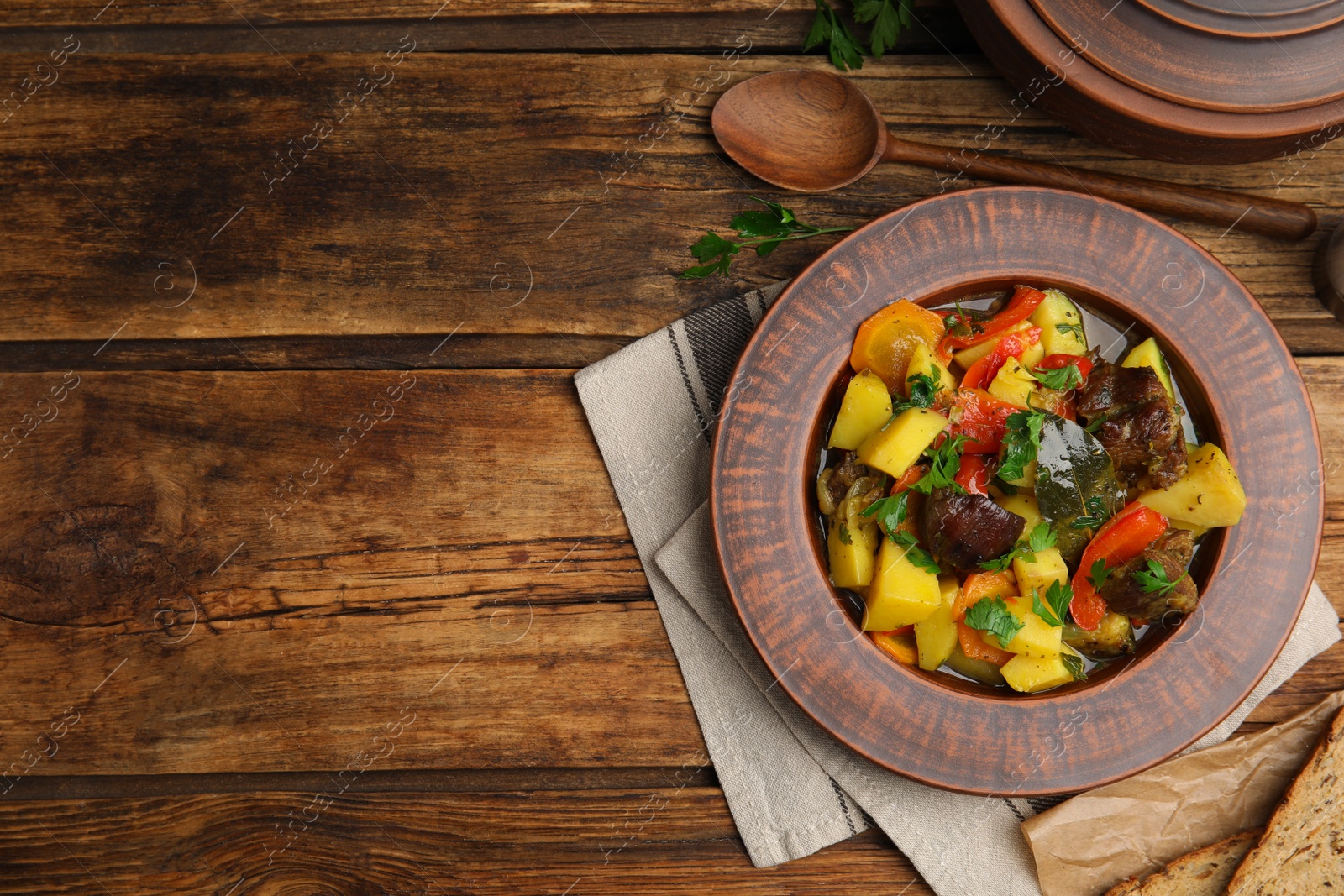 Photo of Tasty cooked dish with potatoes in earthenware served on wooden table, flat lay. Space for text