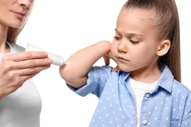 Mother applying ointment onto her daughter's elbow against white background
