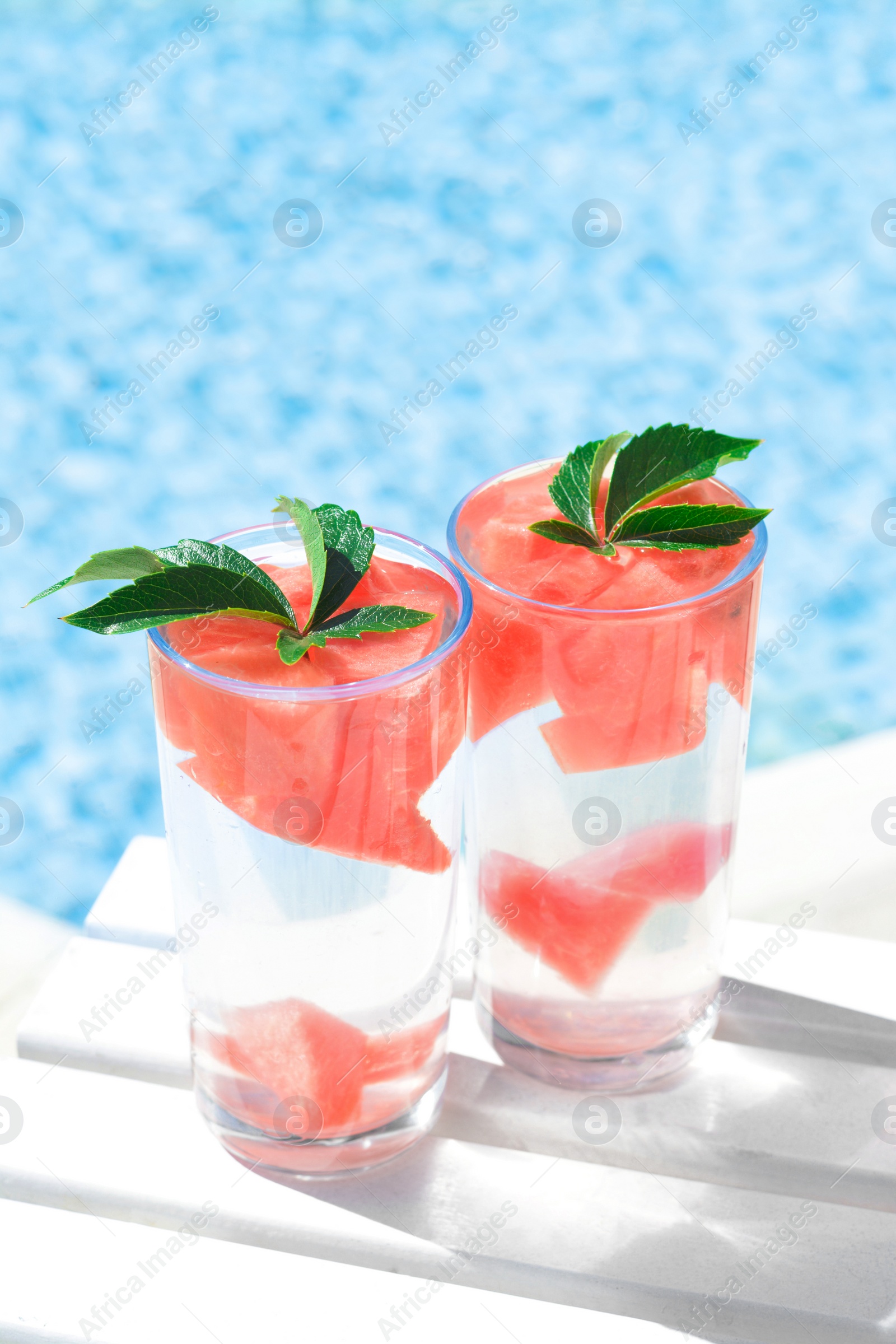 Refreshing watermelon drink in glasses near swimming pool outdoors Photo of Refreshing watermelon drink in glasses near swimming pool outdoors