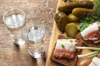 Photo of Cold Russian vodka with snacks on wooden table, above view