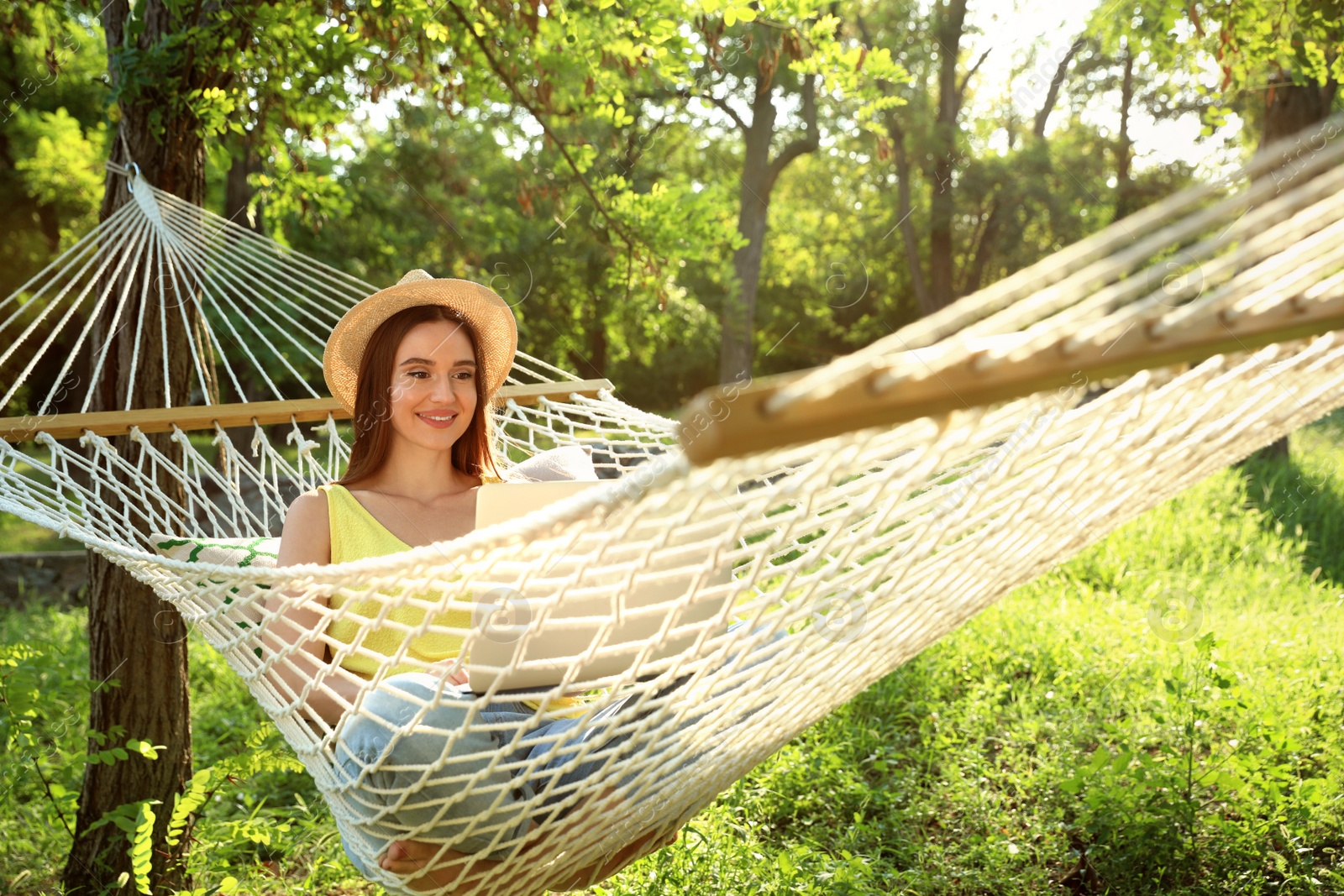 Photo of Young woman with laptop resting in comfortable hammock at green garden