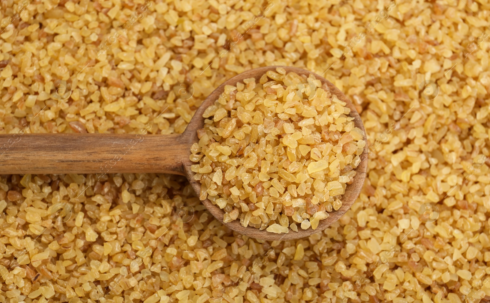 Photo of Wooden spoon on pile of uncooked bulgur, top view