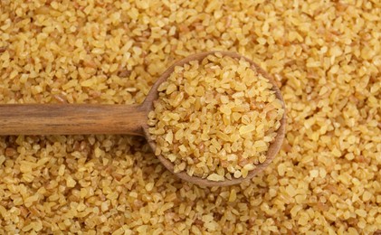 Photo of Wooden spoon on pile of uncooked bulgur, top view