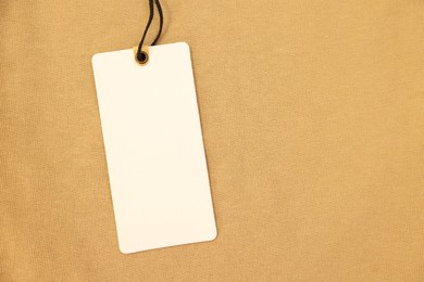 Cardboard tag on beige garment, top view. Space for text