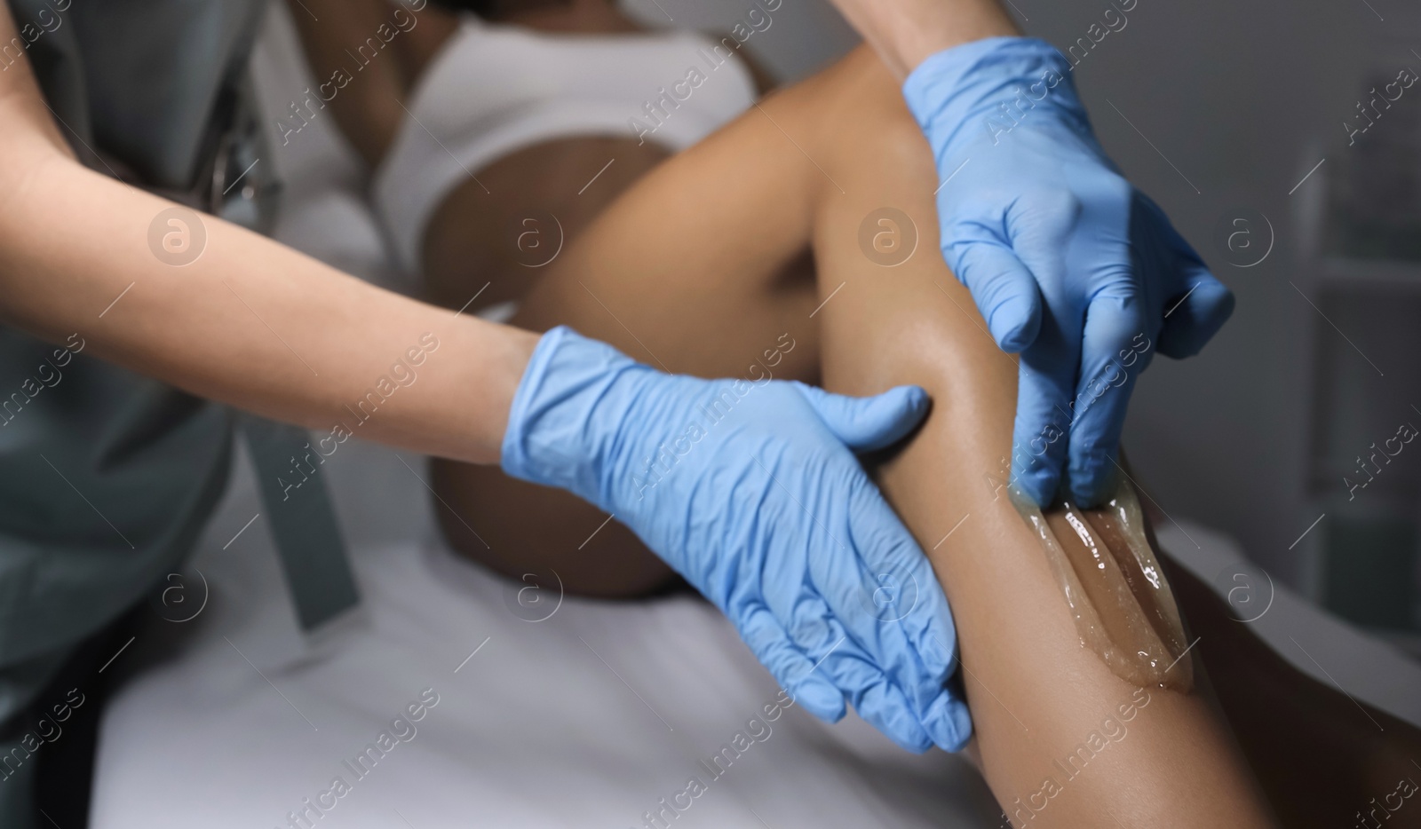 Photo of Young woman undergoing hair removal procedure on legs with sugaring paste in salon, closeup