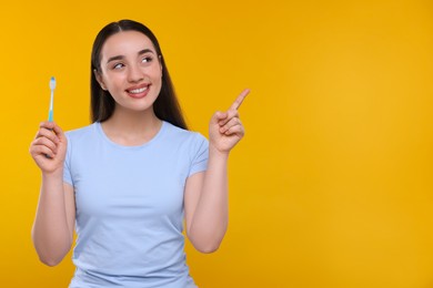 Happy young woman holding plastic toothbrush and pointing on yellow background, space for text