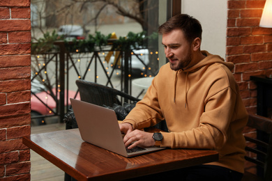 Photo of Male blogger working with laptop at table in cafe