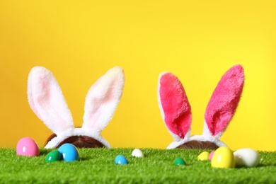 Photo of Easter eggs on green lawn and little girls wearing headbands with bunny ears against color background