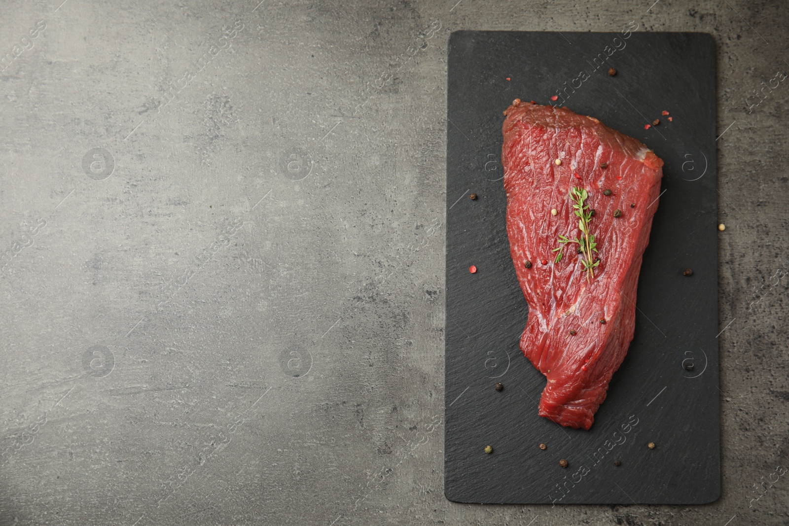 Photo of Fresh raw beef cut with thyme and peppers mix on grey table, top view. Space for text