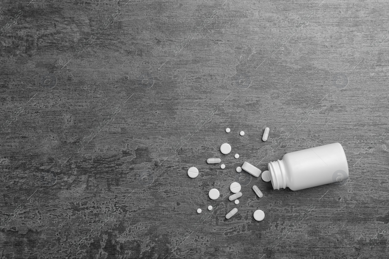 Photo of Container with white pills on grey background