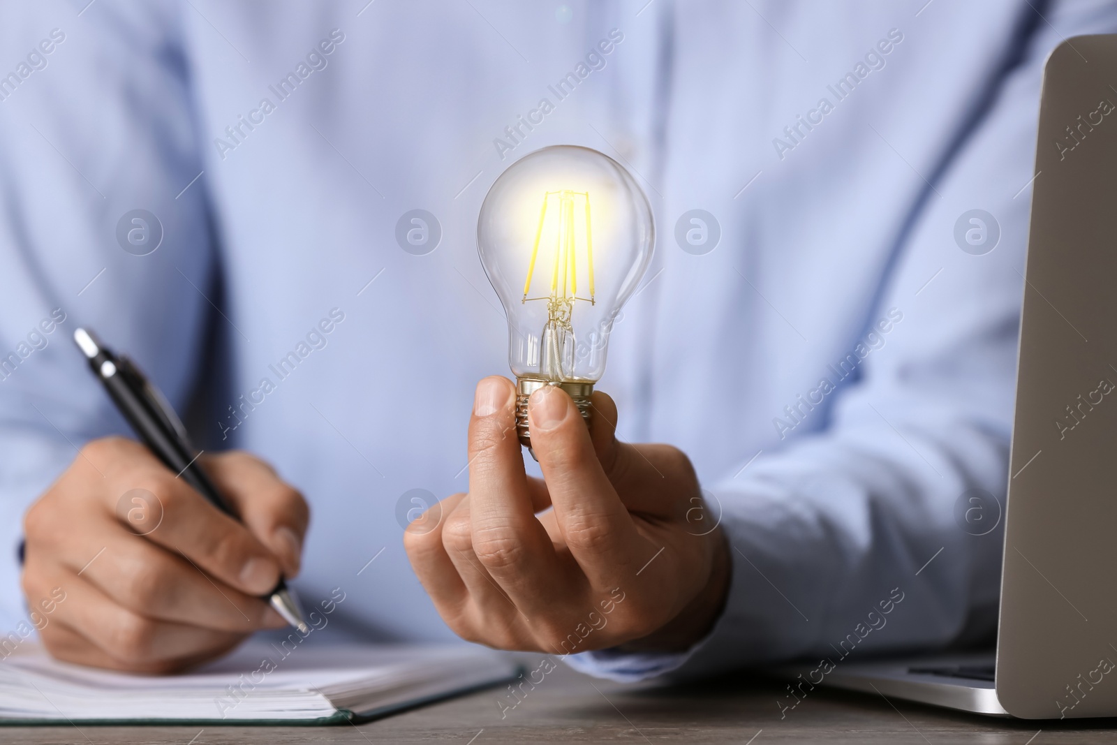 Photo of Glow up your ideas. Closeup view of man holding light bulb while working at wooden desk