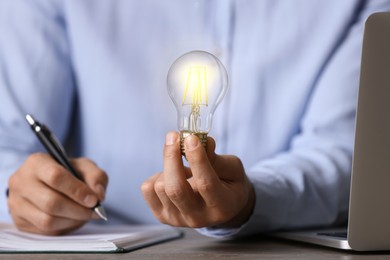 Photo of Glow up your ideas. Closeup view of man holding light bulb while working at wooden desk