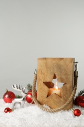 Composition with wooden Christmas lantern on snow against light grey background, space for text