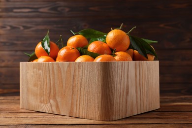 Photo of Fresh tangerines with green leaves in crate on wooden table