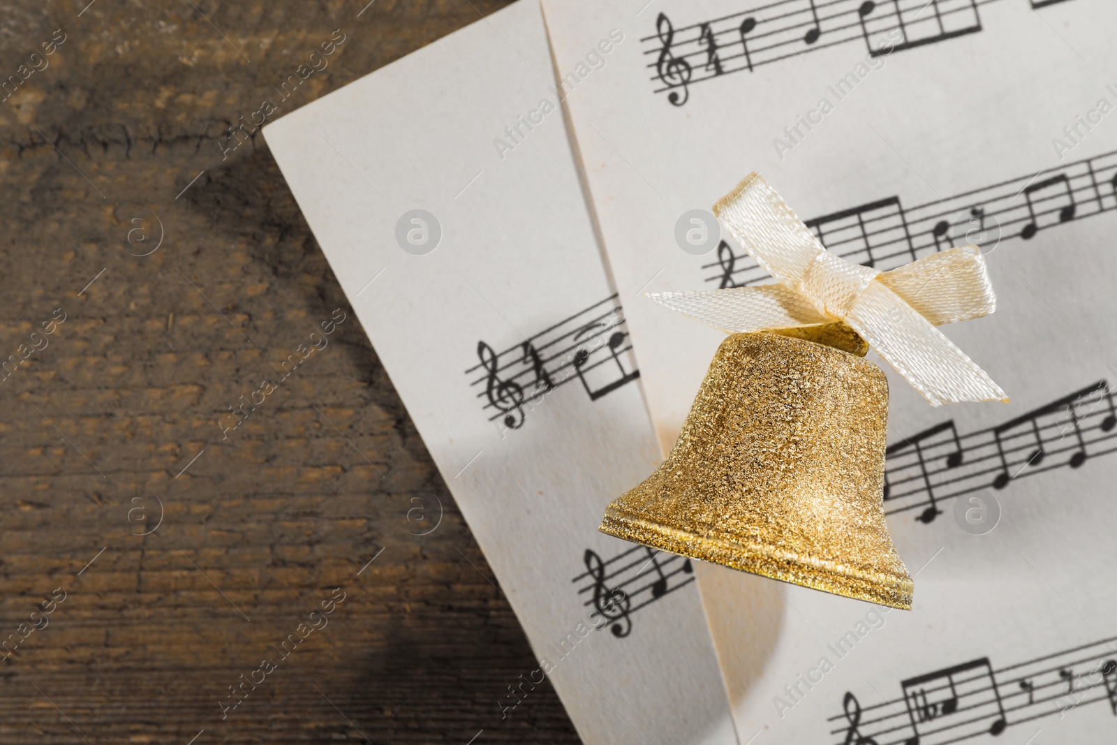 Photo of Golden bell and music sheets on wooden table, flat lay with space for text. Christmas decor