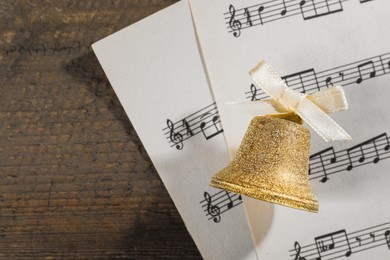 Photo of Golden bell and music sheets on wooden table, flat lay with space for text. Christmas decor