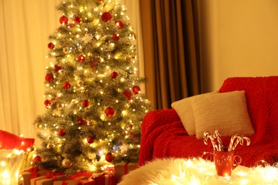 Red cup with candy canes on faux fur in room decorated for Christmas. Interior design