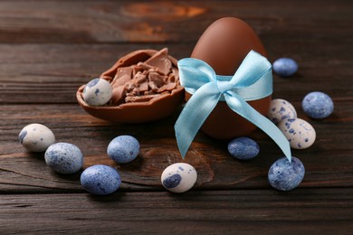 Tasty chocolate egg with light blue bow and sweets on wooden table