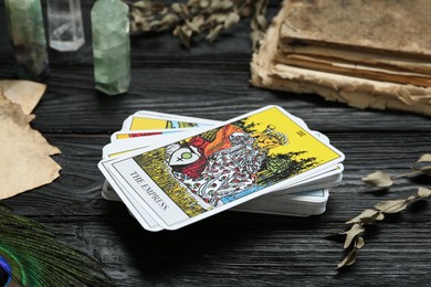 Photo of Tarot cards, old book, crystals and peacock feather on black wooden table, closeup