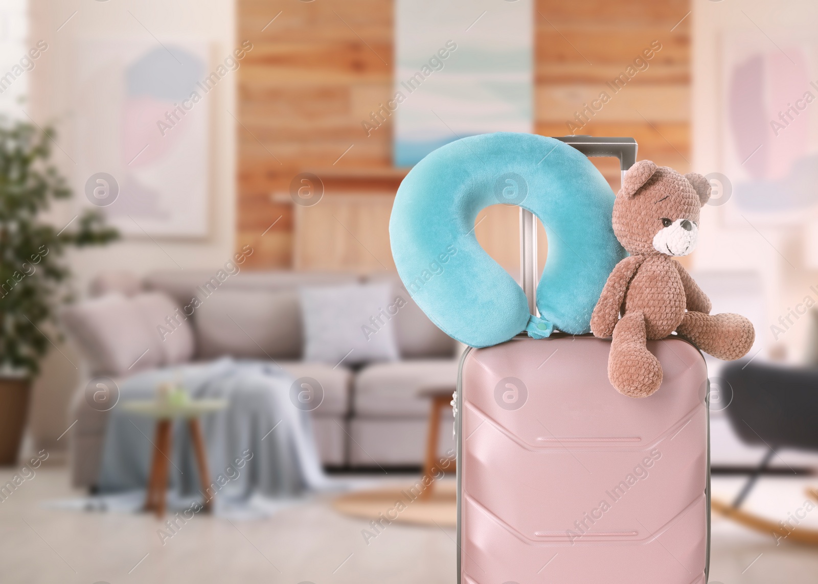 Image of Travel pillow and teddy bear on suitcase in room. Space for text