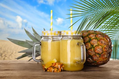 Image of Tasty pineapple smoothie in mason jars on wooden table at beach