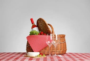 Photo of Picnic basket with wine and products on checkered tablecloth against white background