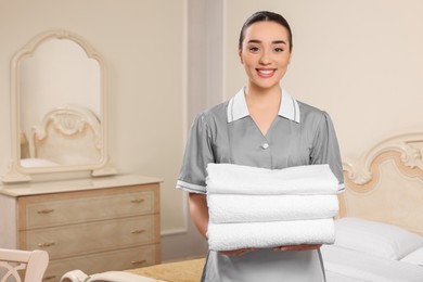 Photo of Young chambermaid holding stack of clean towels in hotel room. Space for text