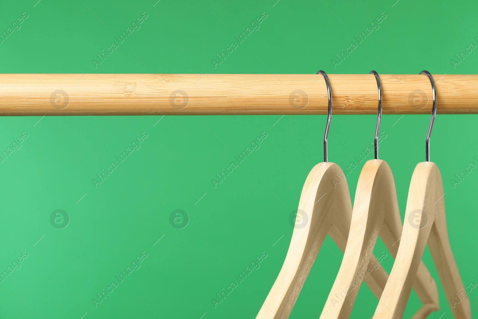 Photo of Empty clothes hangers on wooden rack against green background, closeup. Space for text