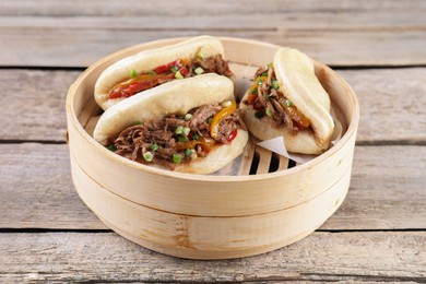 Photo of Delicious gua bao in bamboo steamer on wooden table