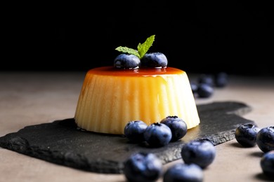 Delicious caramel pudding with blueberries and mint on grey table against black background, closeup