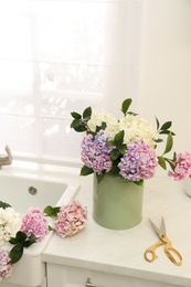 Photo of Bouquet with beautiful hydrangea flowers in can and scissors on light countertop