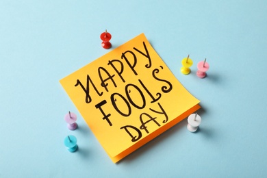 Photo of Sticky note with phrase Happy Fools' Day and push pins on light blue background