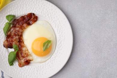 Fried egg, bacon and basil on light grey table, top view. Space for text