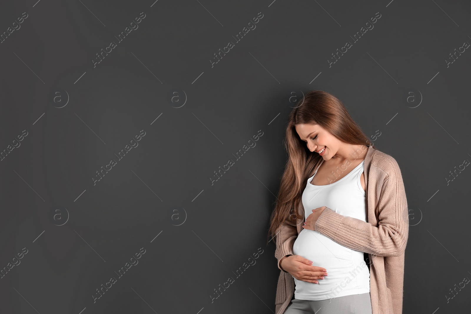 Photo of Young pregnant woman on grey background. Space for text