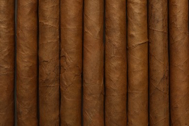 Many cigars wrapped in tobacco leaves as background, top view