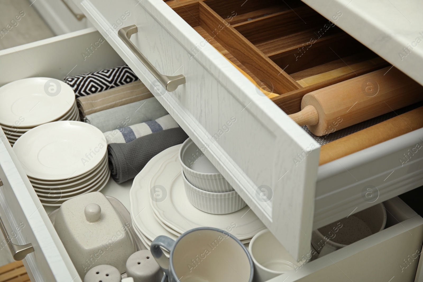 Photo of Open drawers of kitchen cabinet with different dishware, utensils and towels