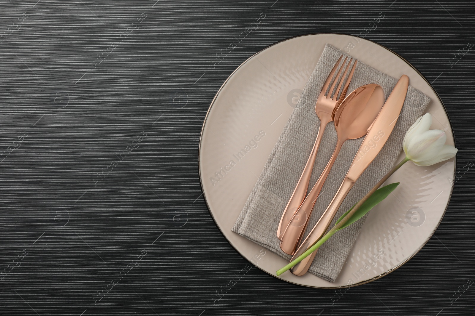 Photo of Stylish setting with cutlery, flower and plate on black wooden table, top view. Space for text