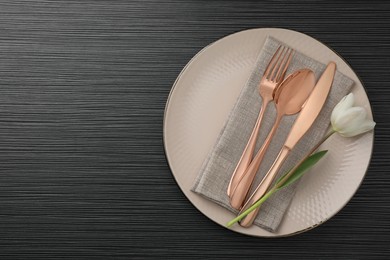 Stylish setting with cutlery, flower and plate on black wooden table, top view. Space for text