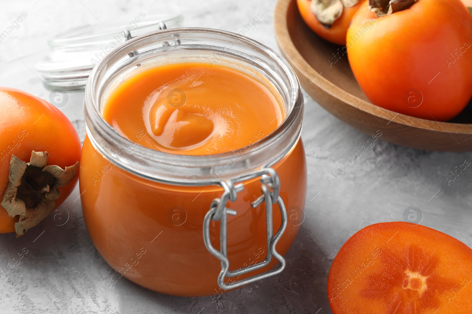 Photo of Delicious persimmon jam and fresh fruits on grey table, closeup