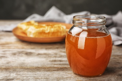 Photo of Glass jar with sweet honey on wooden table, closeup