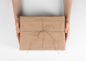 Photo of Woman holding parcel wrapped in kraft paper on white background, top view