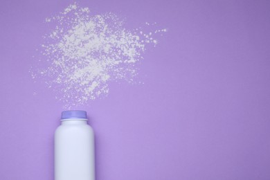 Bottle and scattered dusting powder on violet background, top view with space for text. Baby cosmetic product