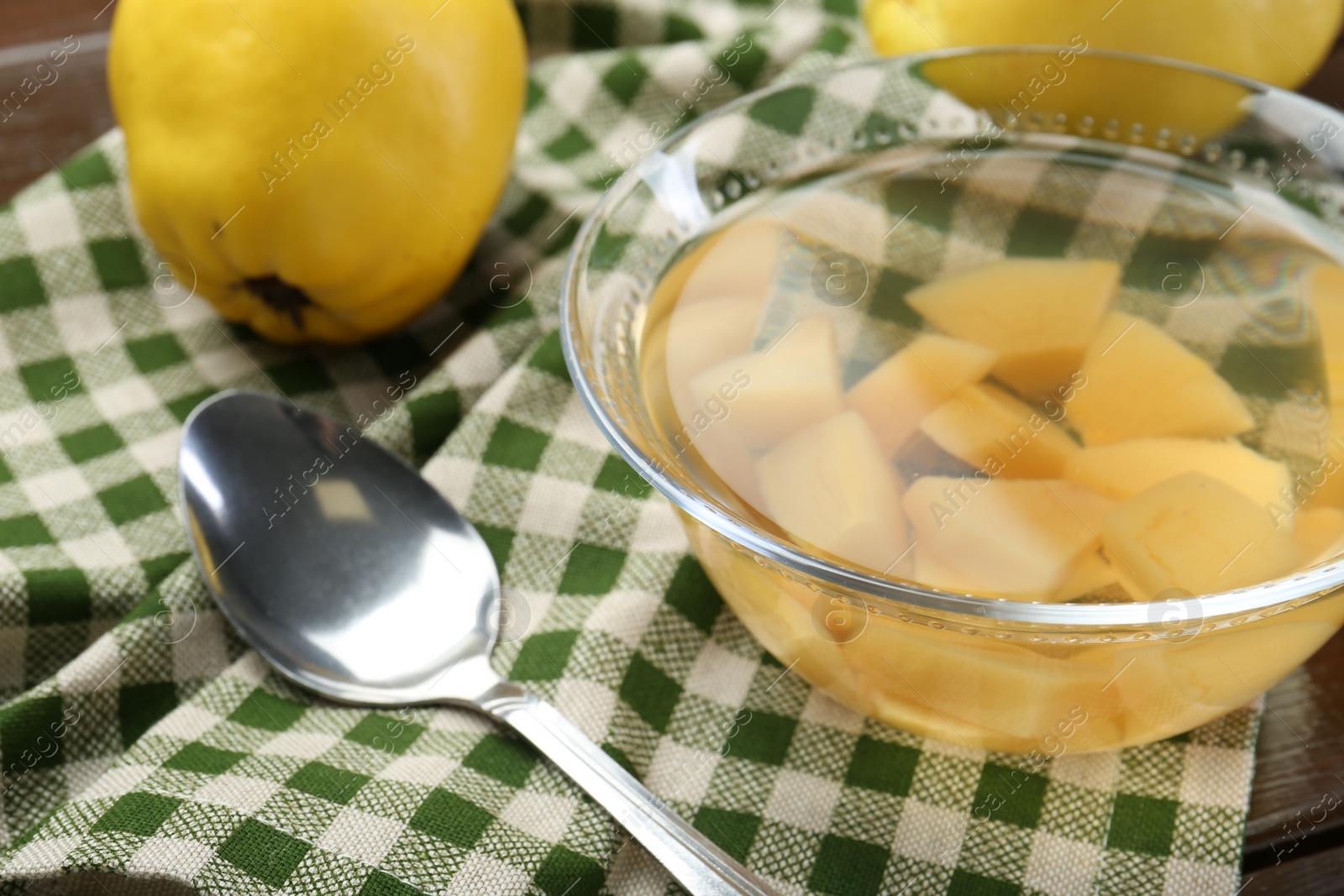 Photo of Delicious quince drink in glass bowl, fresh fruit and spoon on table, closeup