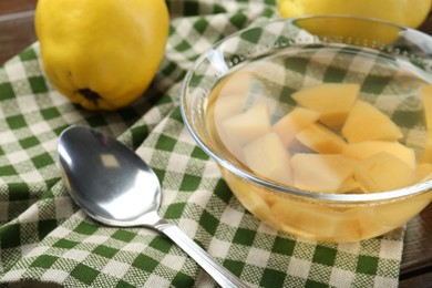 Photo of Delicious quince drink in glass bowl, fresh fruit and spoon on table, closeup