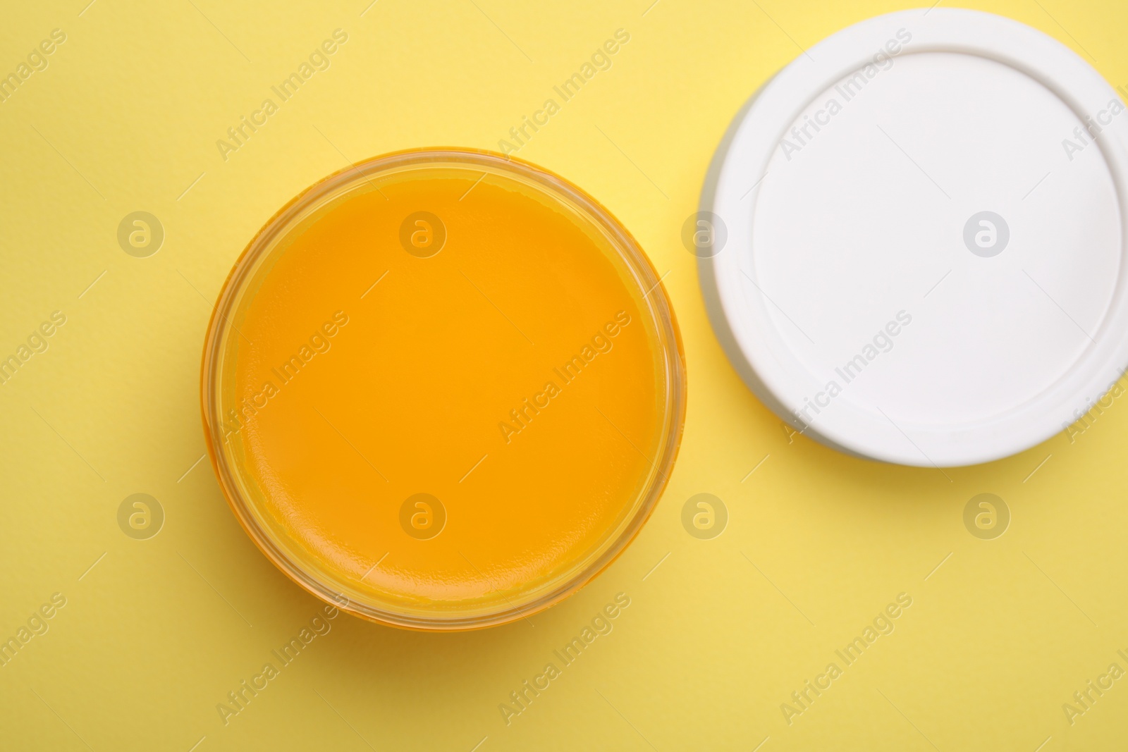 Photo of Open jar of petrolatum on yellow background, top view