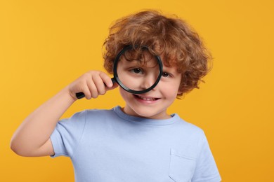 Photo of Cute little boy looking through magnifier glass on orange background