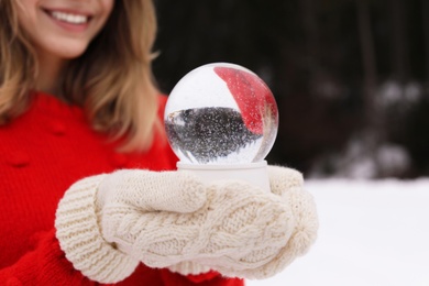 Woman with knitted mittens holding snow globe outdoors, closeup