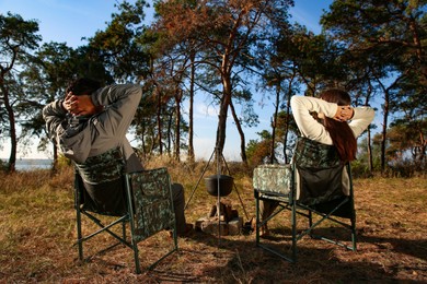 Couple resting in camping chairs outdoors, back view