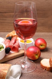 Glass of delicious rose wine and snacks on wooden table
